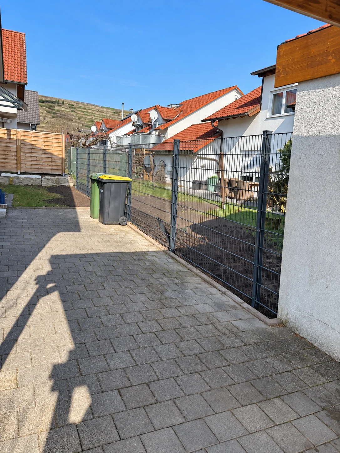 Stabmattenzaun mit Tor an einer gepflasterten Zufahrt.